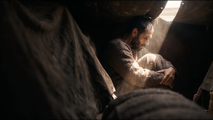 Saúl, encogido entre los bultos del equipaje, con una rendija de luz
